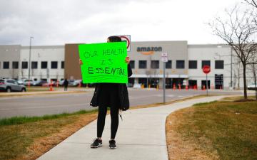 worker stands outside Amazon building holding a sign that reads, 