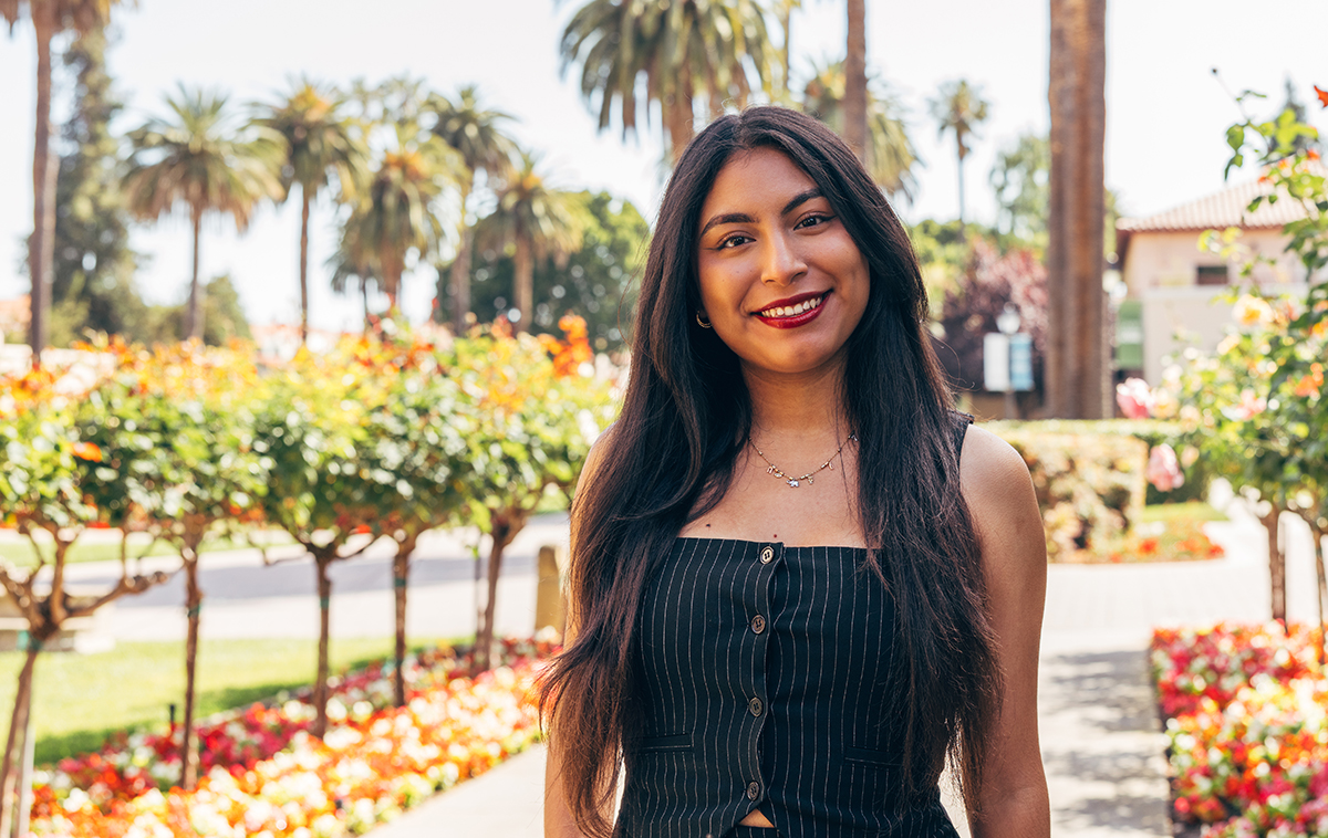 Julissa Martinez standing on walkway bordered with blooming flowers, next to Mission Church.