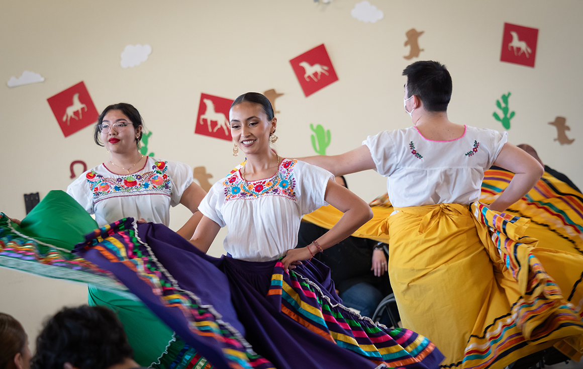 Three students dancing and twirling in colorful Mexican skirts.