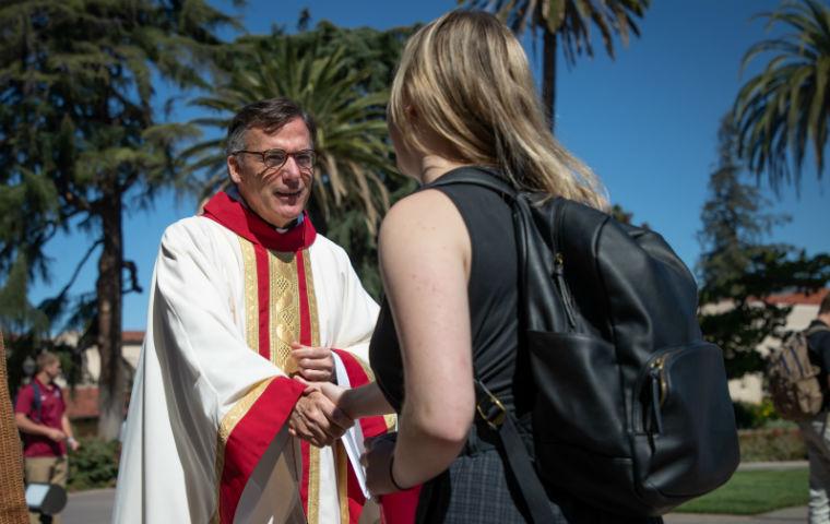 Fr. O'Brien in clerical garb shaking hand of female student, seen from behind student