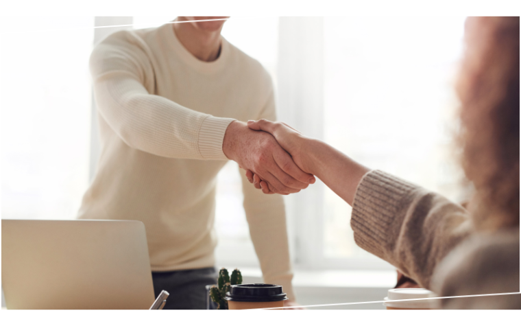 Two people shaking hands over a desk