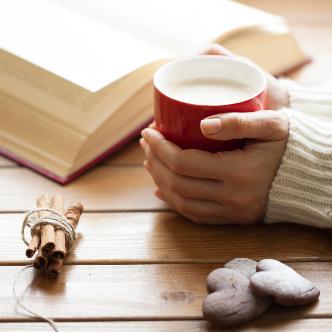 Hands with coffee mug resting on a table, near an open book 