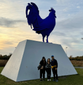 3 people stand in front of the Hahn/Cock sculpture in the Minneapolis sculpture garden