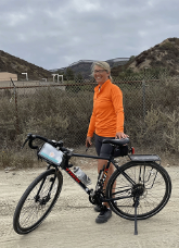 Virginia Matzek with bicycle in front of the Mexican border wall