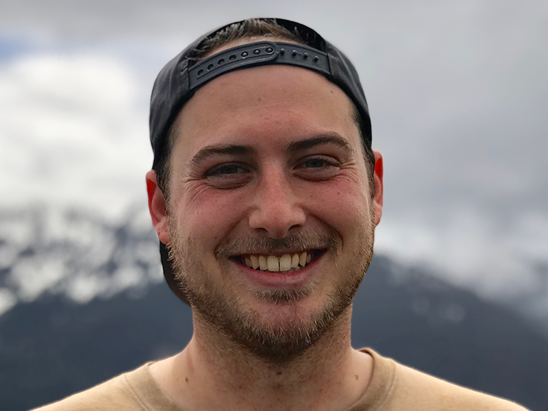 Zach Milkis headshot with mountains and dark clouds in he background