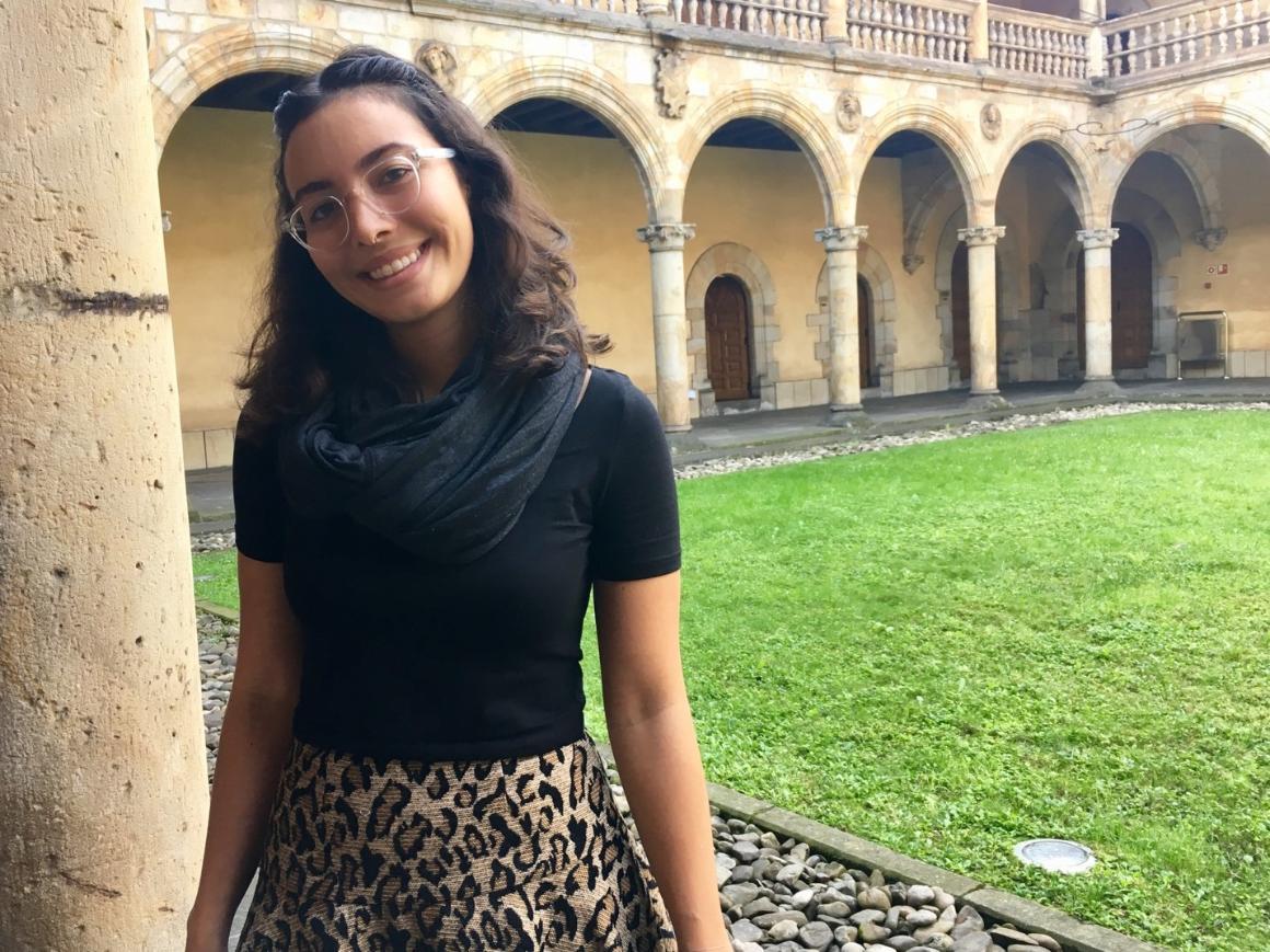 A person smiling in a historical courtyard with arches.