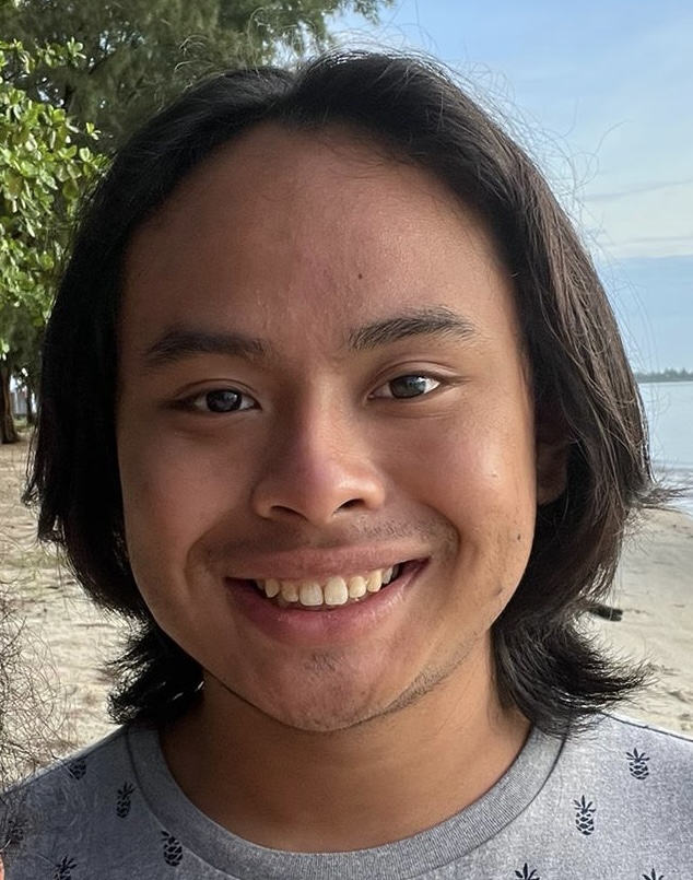 A person smiling outdoors near the sea.