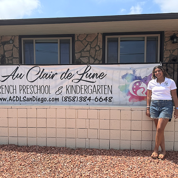 Sarah Benmalek standing next to the Au Clair de Lune banner.