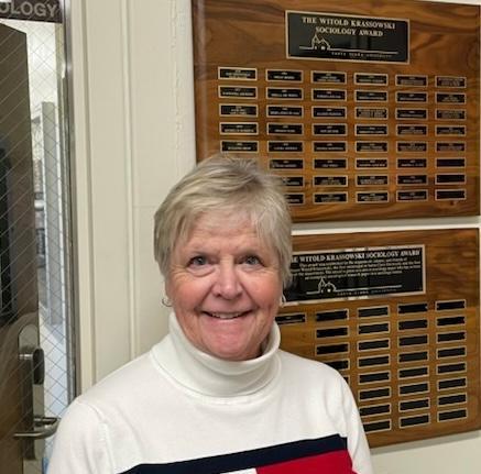 Mary McLane in front of Krassowski award plaque in the Sociology Lounge