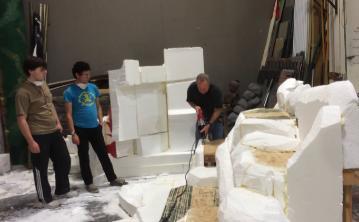 Three people observing white sculptural models inside a studio. 