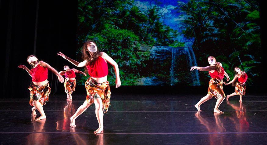 5 female dancers in red costumes performing on stage with tropical backdrop