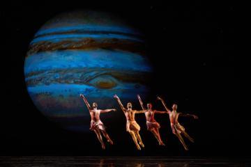 4 ballerinas jumping in cabriole against a projection of Jupiter