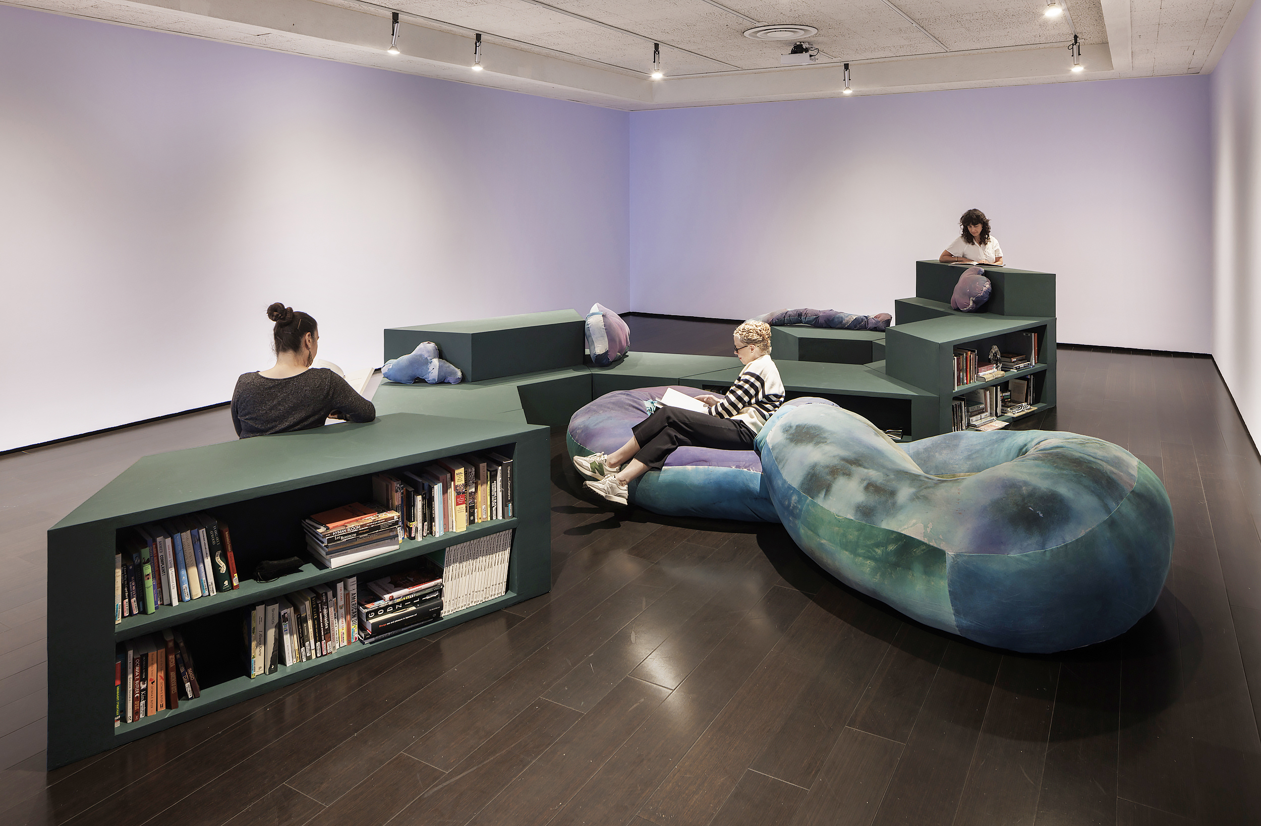 People sitting on modular bookshelf and large cushions reading books