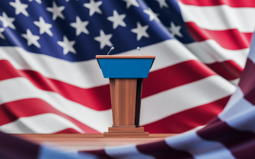 Election debate table over USA flag background By ImageFlow/Adobe Stock.