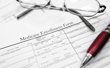 A pair of reading glasses, a pen, and a blank Medicare enrollment form. Credit: zimmytws_Adobe Stock