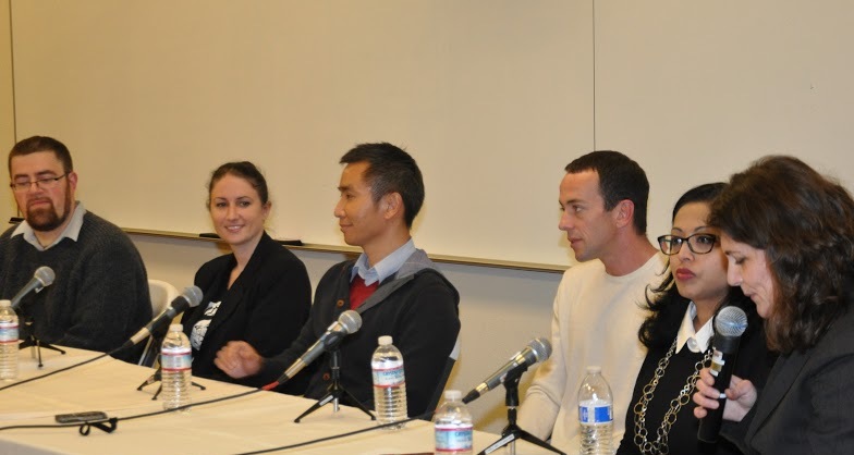 A panel of five people speaking into microphones at a table.