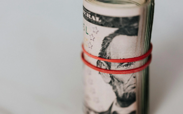 Roll of american dollars tightened with red band. Photo by Karolina Kaboompics_Pexels. image link to story