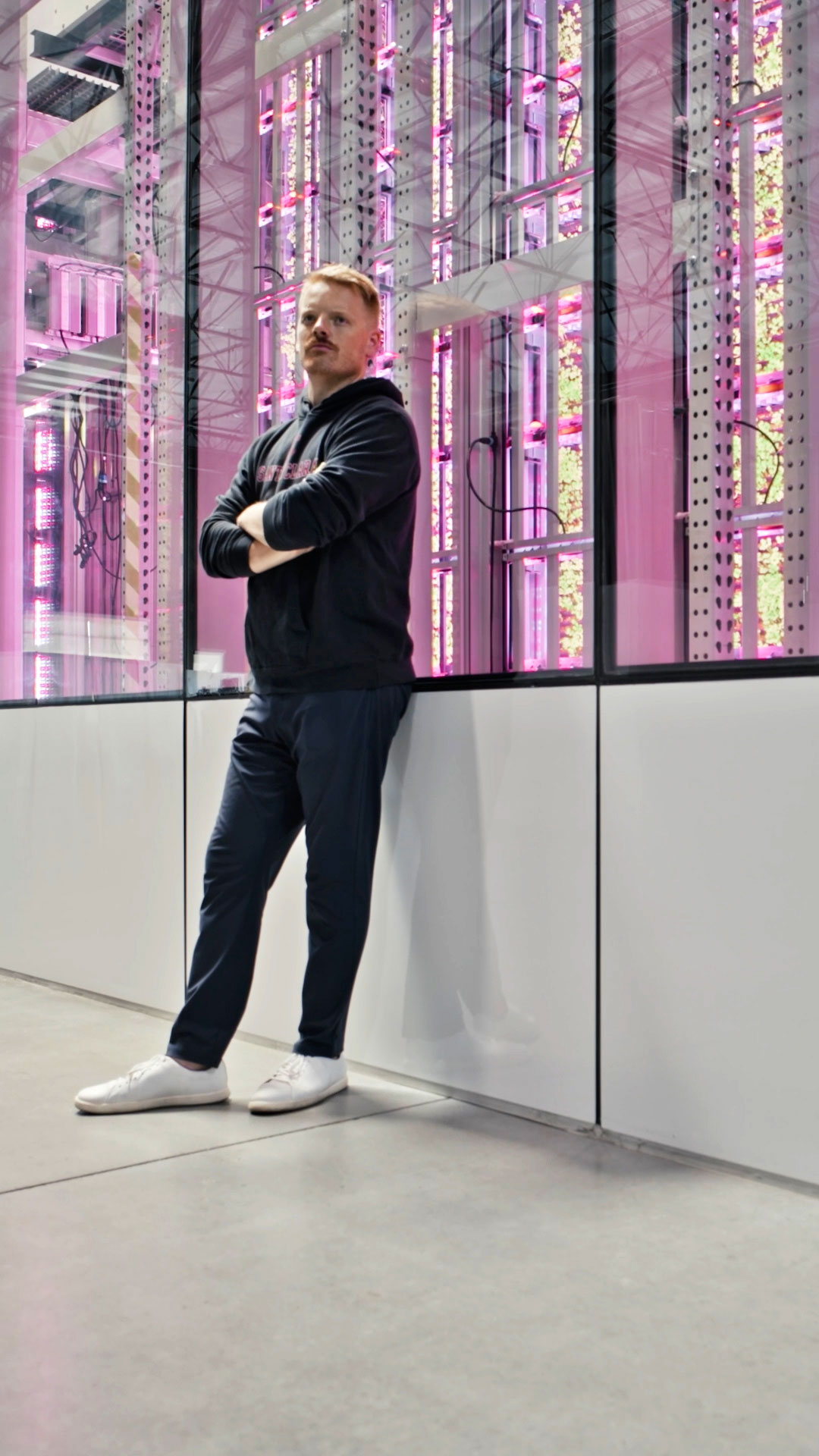 Sam Bertram '16, M.S. '18, with his arms crossed proudly, in front of his vertical farm