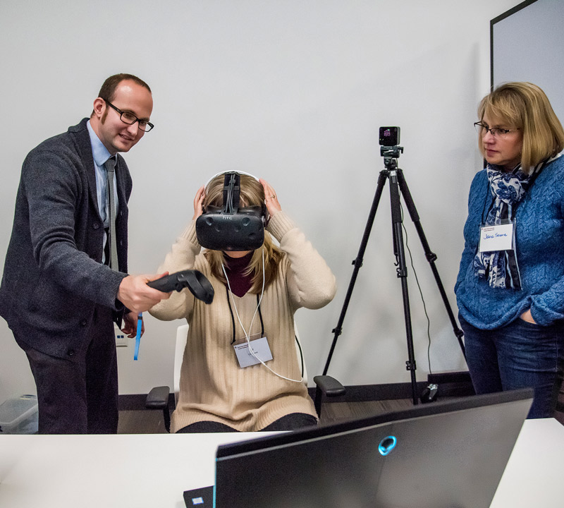 Three adults in a lab, one wearing googles, one assisting, and one observing,  performing simulations