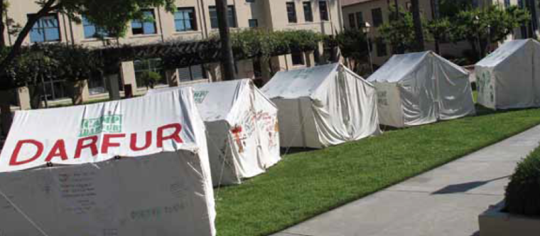 Several tents with writings, set up on a grassy area near buildings.