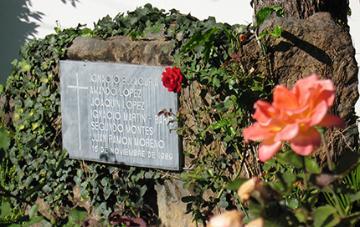 A plaque surrounded by plants, with a rose and an orange flower.