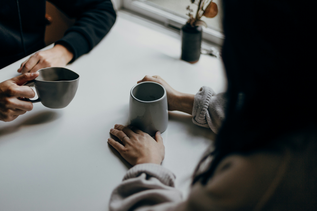 Two individuals sitting across from each other each holding a cup placed on the table 