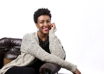 A person sitting on a sofa, smiling, wearing a cardigan.