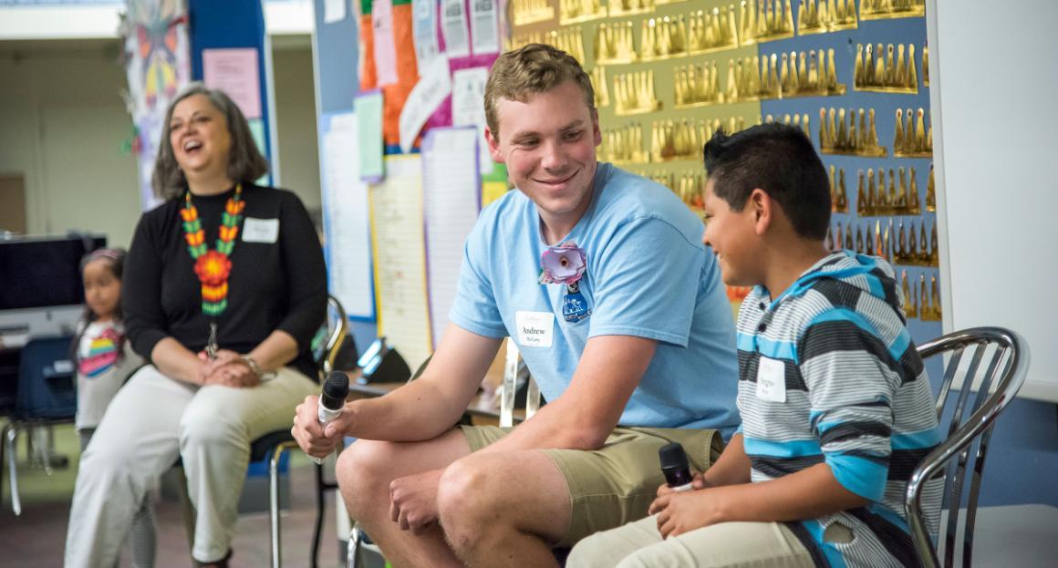 A student volunteer sits next to an elementary student during a presentation 