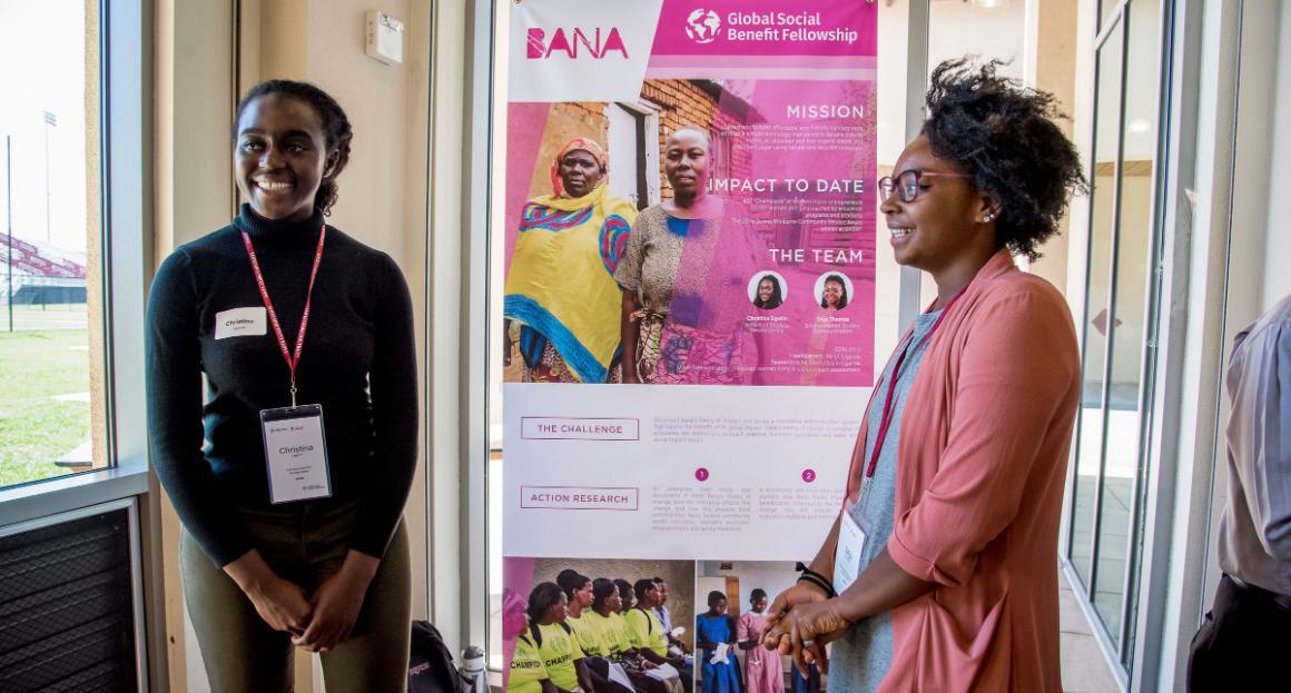 Two students smile as the stand next to their presentation board at a research open house 