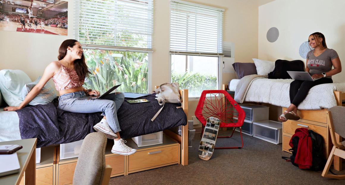 Two student dorm mates sit on their beds while chatting 