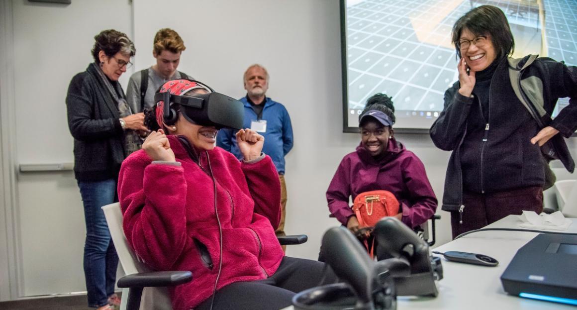 A professor stands by smiling as a student experiences using the VR headset 