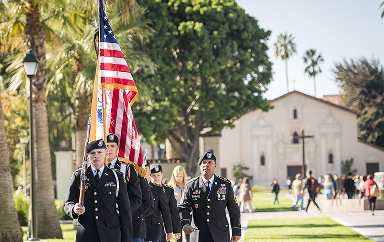 Color guard marching on campus in front of the mission image link to story