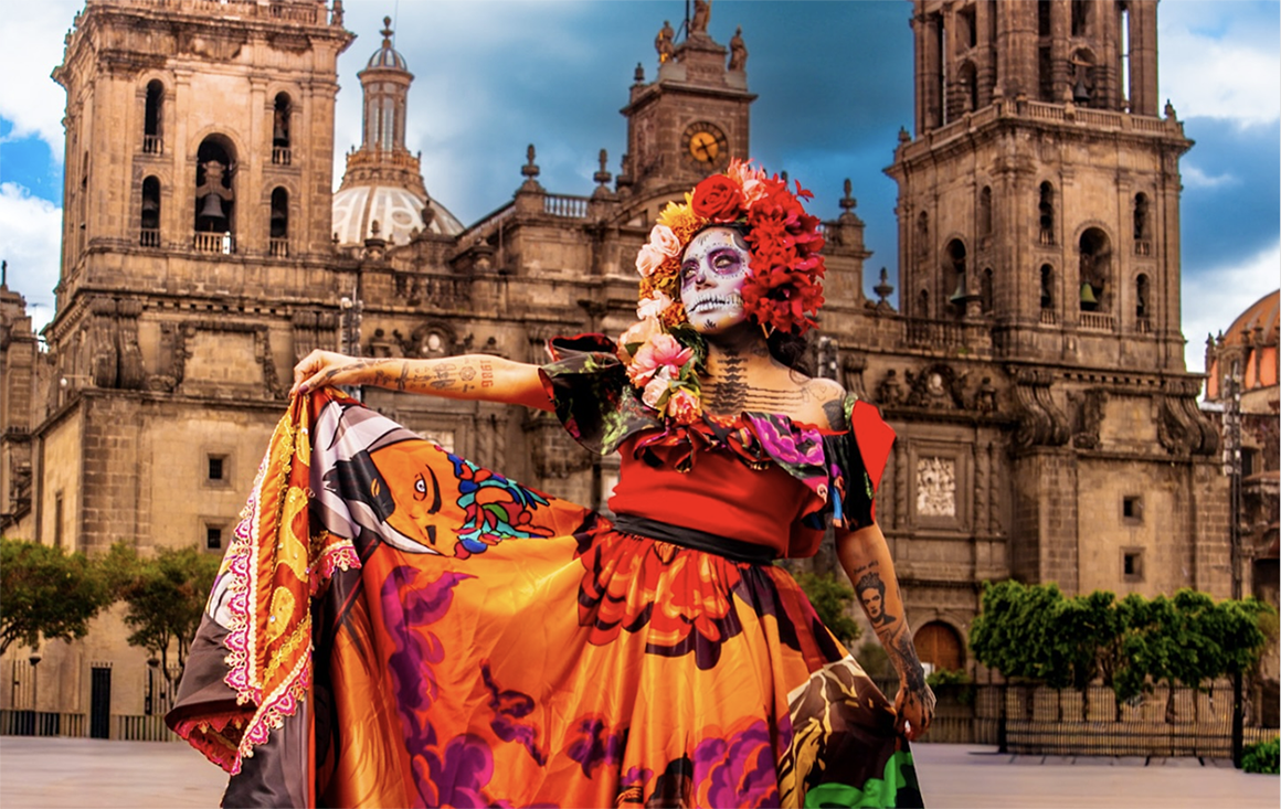 A woman in skeletal makeup, an orange flower crown, and a rich, highly decorated orange dress poses, lifting her skirt in one hand, a large, ornate, European-style stone building in the background.