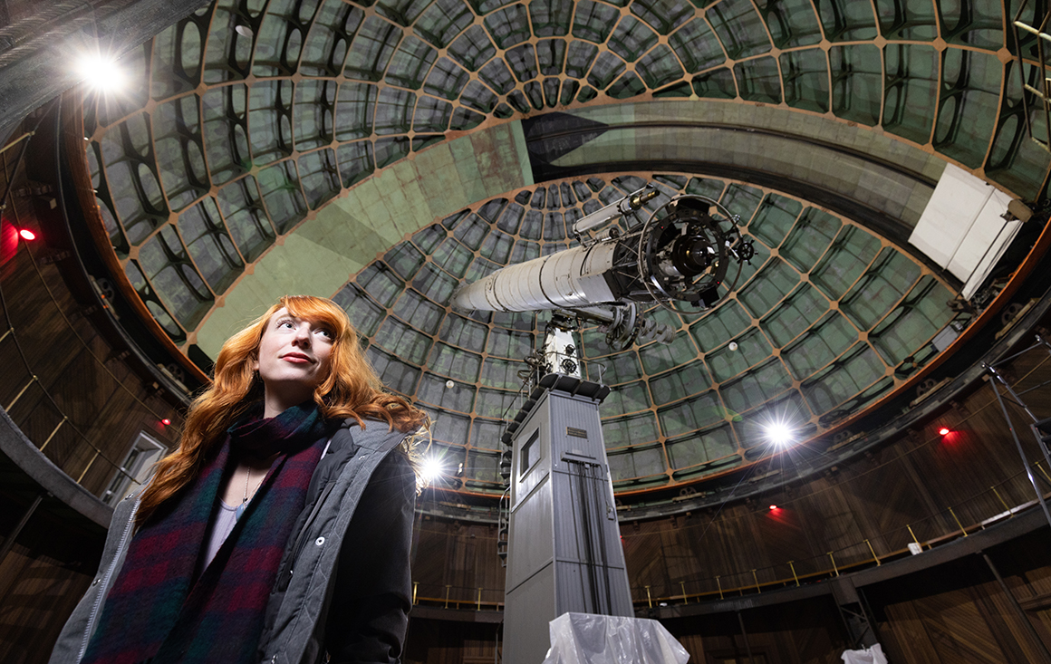 A woman standing below a large astronomical telescope. image link to story