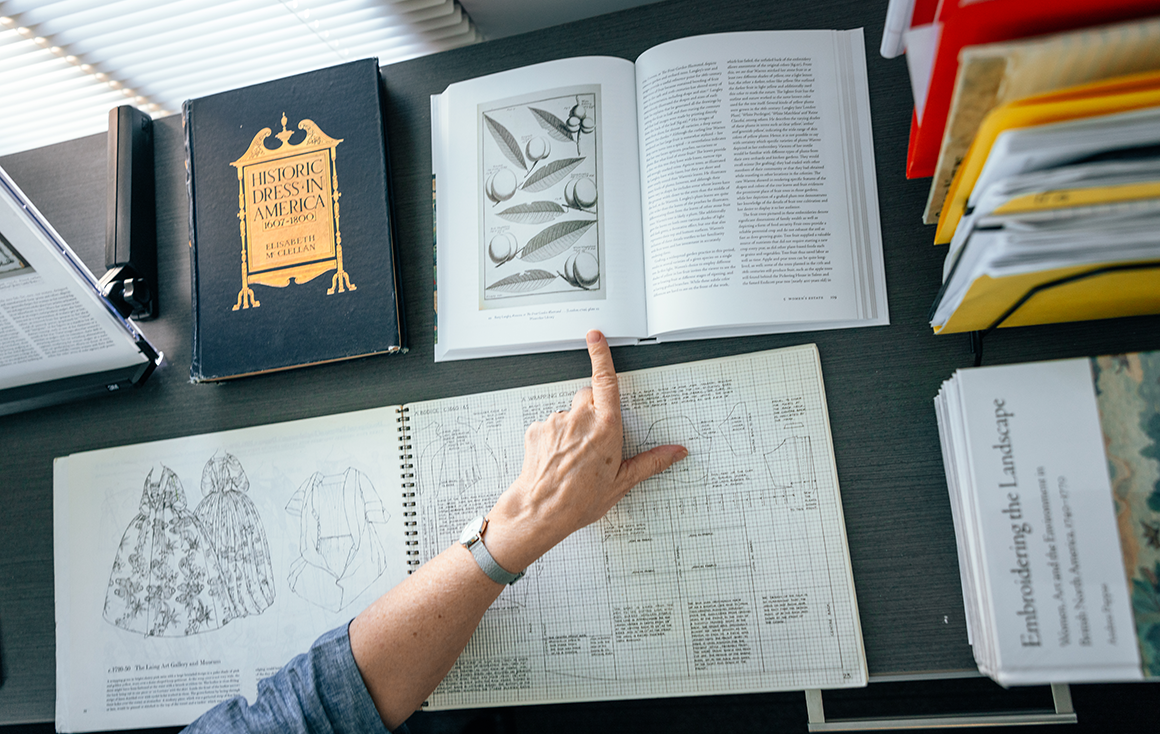 A woman's hand point to a stone fruit illustration in an open book on a desk.