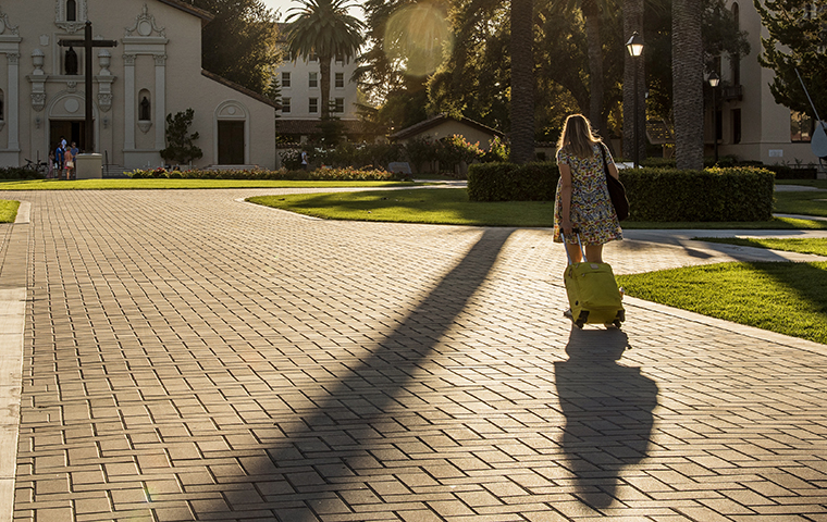 Woman walking into the sunset in front of the Mission with a pull suitcase