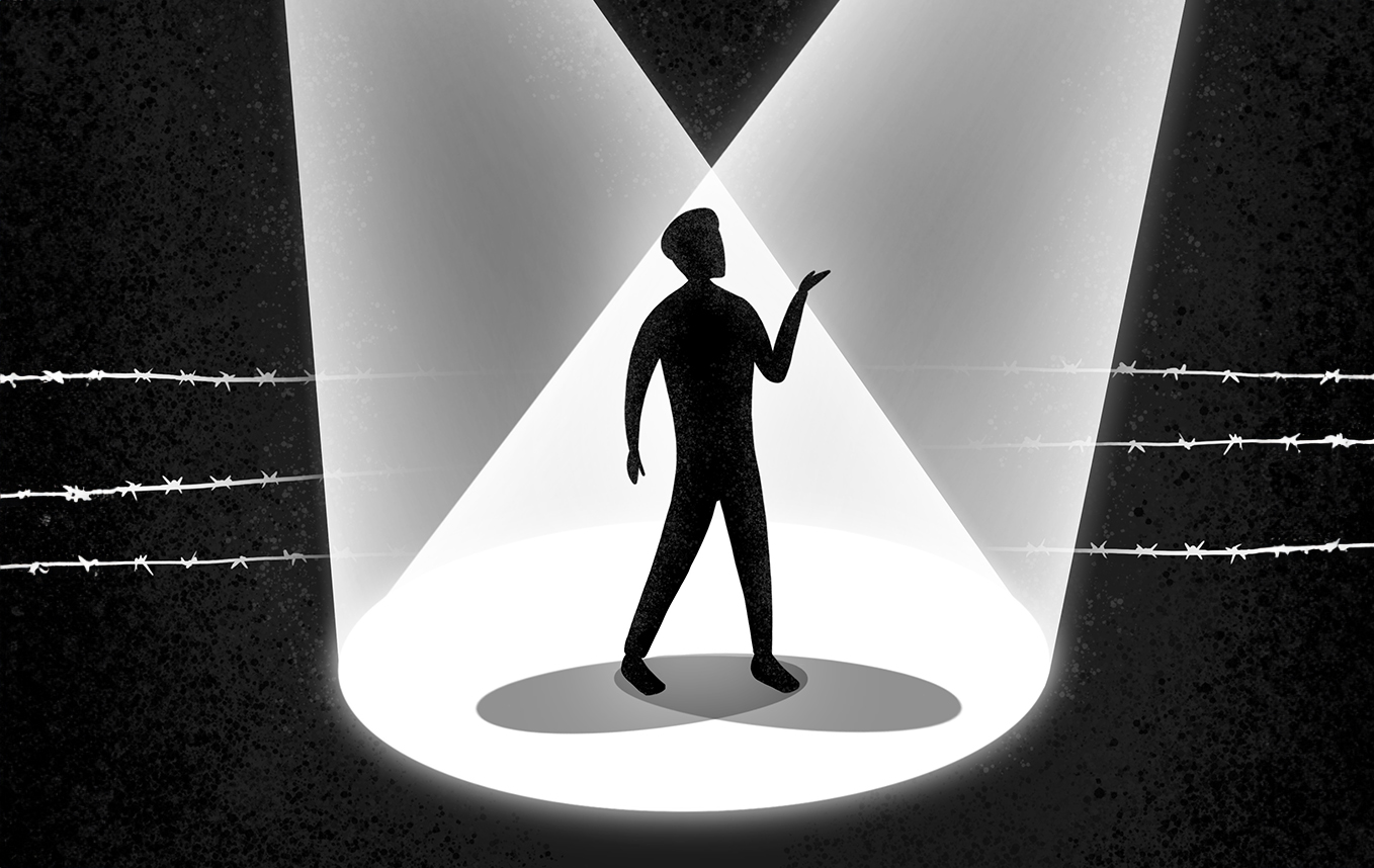 A silhouetted figure stands under two crossed theater spotlights, with faint white barbed wires running horizontally in the distant, black background.