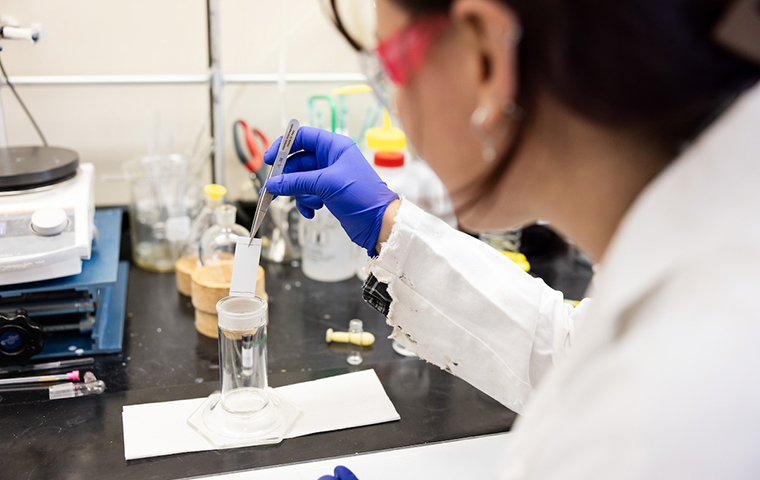 Image of scientist in lab using tongs to remove paper from a vial.