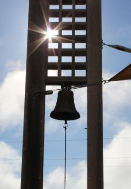 A bell hanging from a tall structure with a sunny sky background.