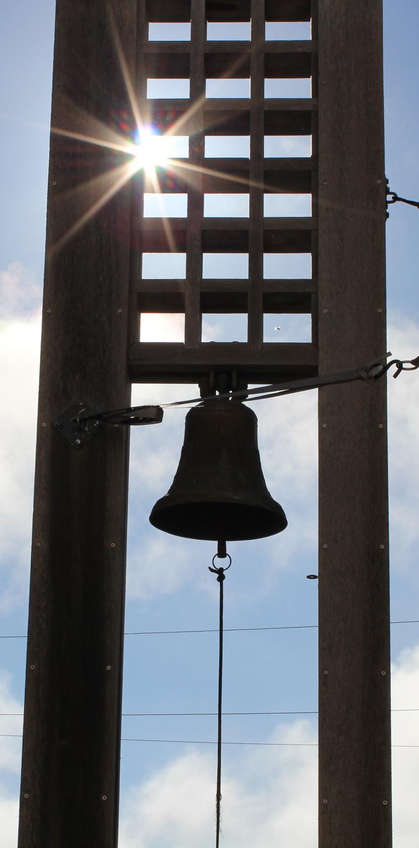 A bell hanging from a tall structure with a sunny sky background.