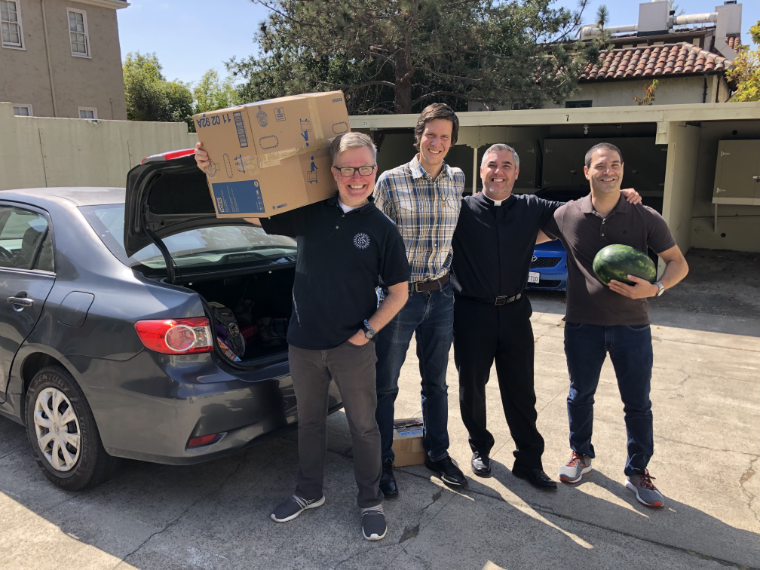 Four men loading car trunk with boxes and bags labeled 