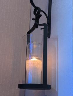 Lit candle in glass holder mounted on a wall with a metal bracket.