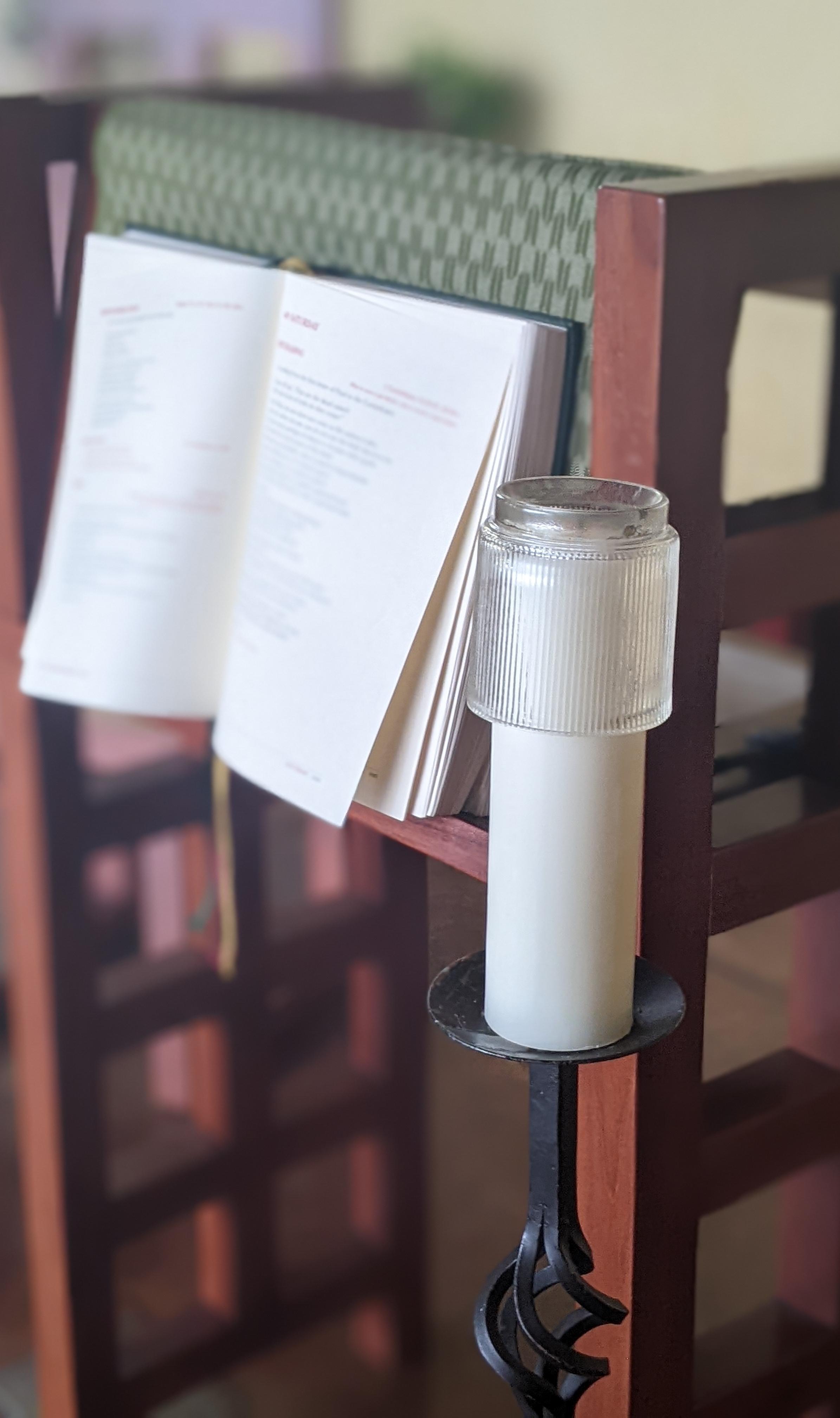 Open Bible and candle on a wooden stand.