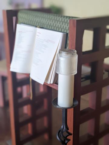Open Bible and candle on a wooden stand.