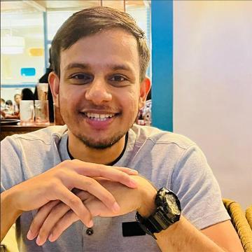 Young man smiling seated at a table with his hand crossed in front of him