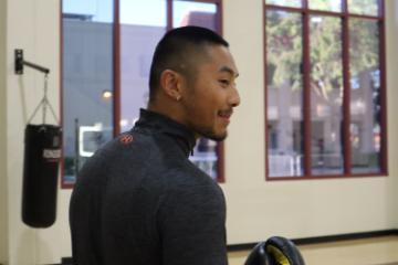 A person in a gym wearing a dark-colored shirt, with gym equipment visible.