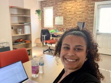 A woman smiling in an office with a brick wall.