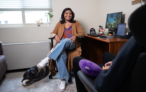 Woman sitting in chair with a dog at her feet.