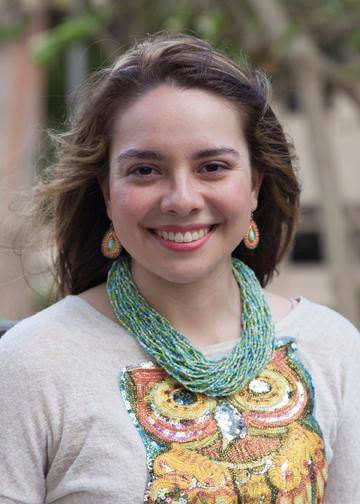 A person wearing a colorful necklace and decorated shirt, smiling at the camera.