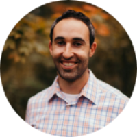 A man smiling with a blurred nature background.